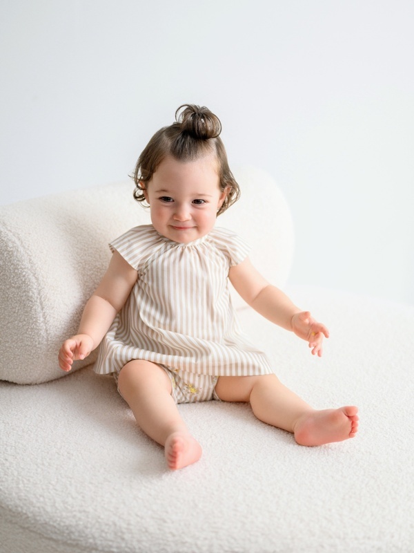 Bebé sentada sonriente vistiendo un jesusín de rayas de la colección Malefica Rayas de Babydif, perfecto para un look marinero, fresco y fotogénico.
